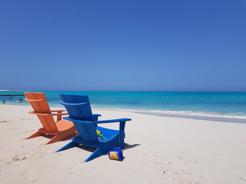 Orange and blue beach chairs on white sand facing turquoise sea.
